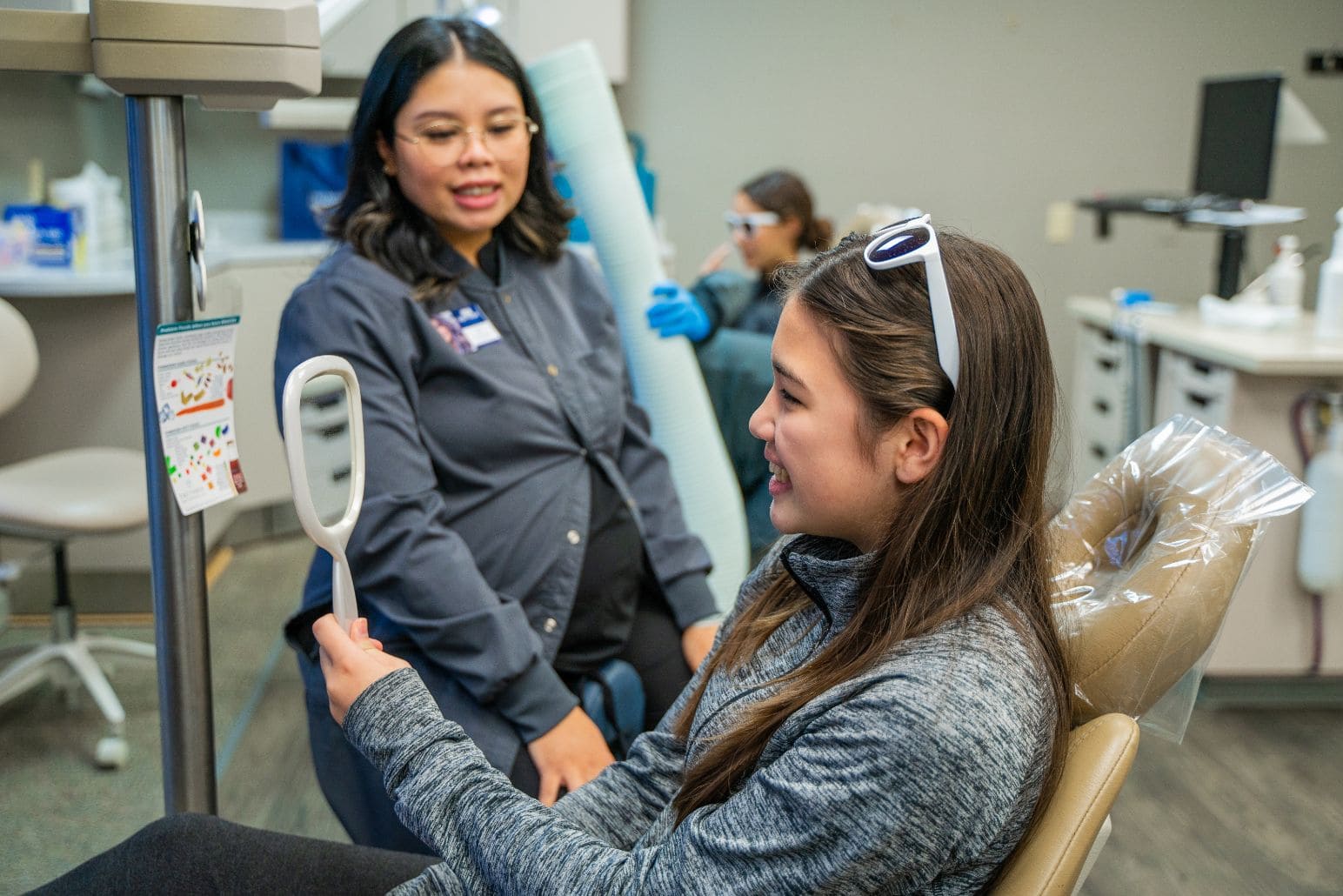 A woman is sitting in a treatment chair looking in a mirror.