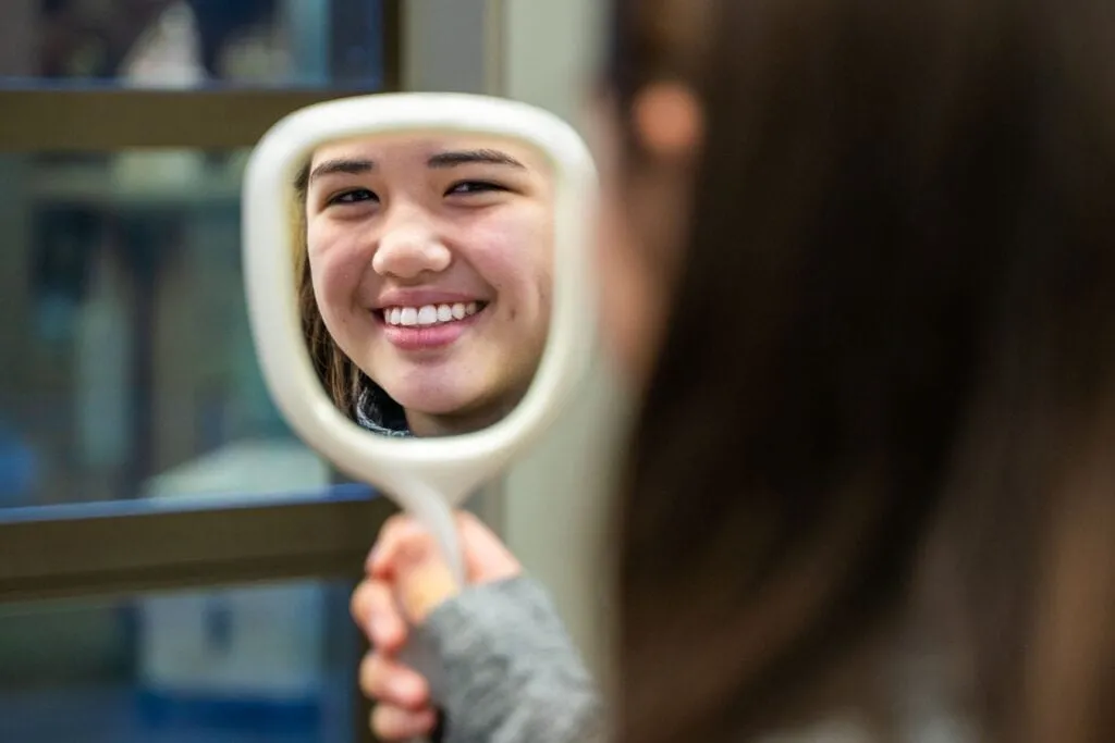 A young woman looking at herself in a mirror.