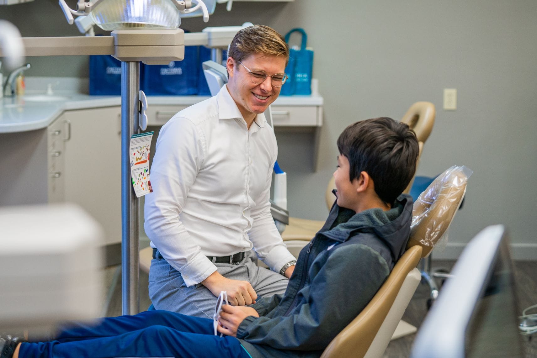 Dr. Adam talking to a young boy patient in a treatment chair.