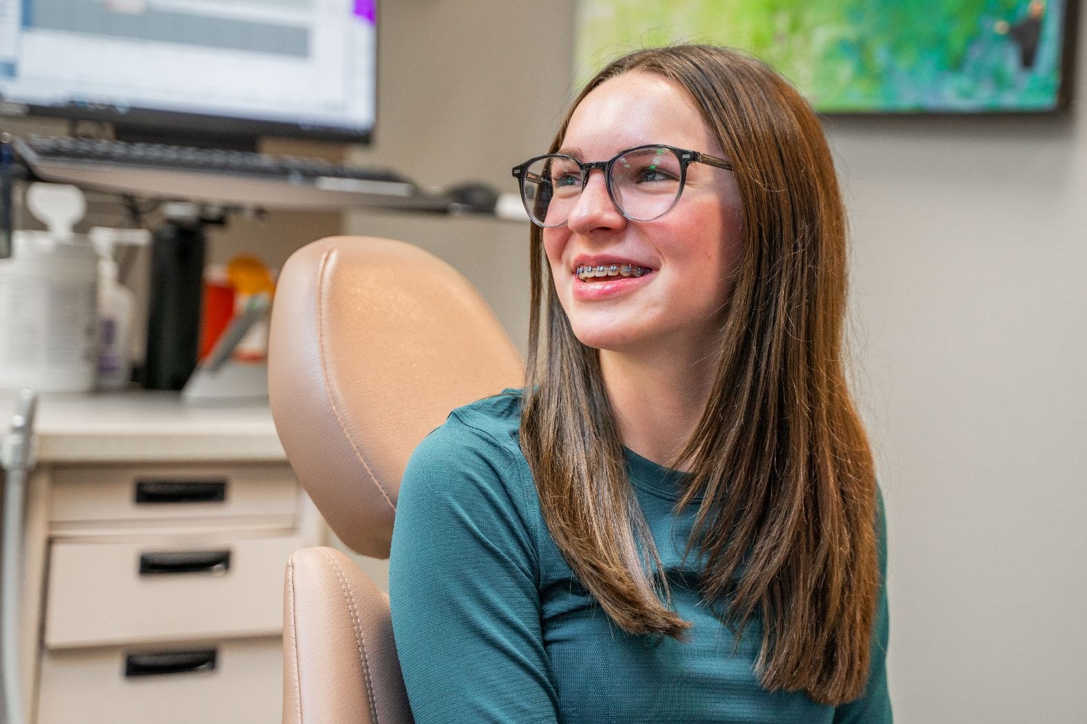 A teen girl smiles while sitting in a dental chair.